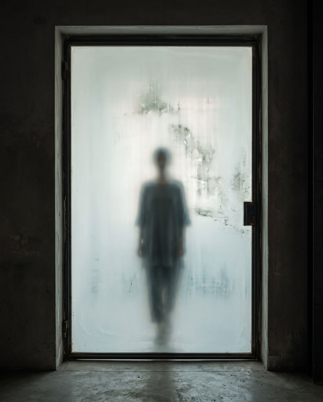 Anonymous female silhouette seen only through an opaline glass doorway.